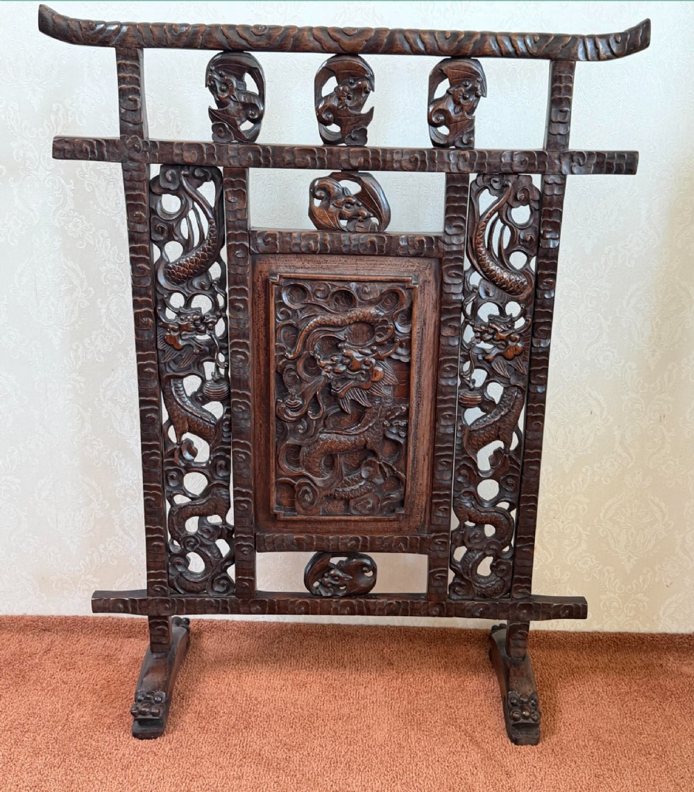 A dark carved hardwood freestanding screen featuring openwork dragon motifs and a central relief panel on carved feet.
