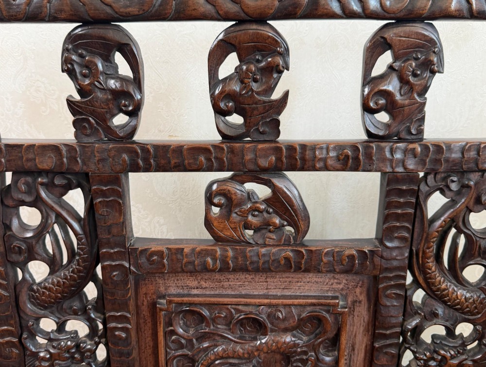 A dark carved hardwood freestanding screen featuring openwork dragon motifs and a central relief panel on carved feet. View II