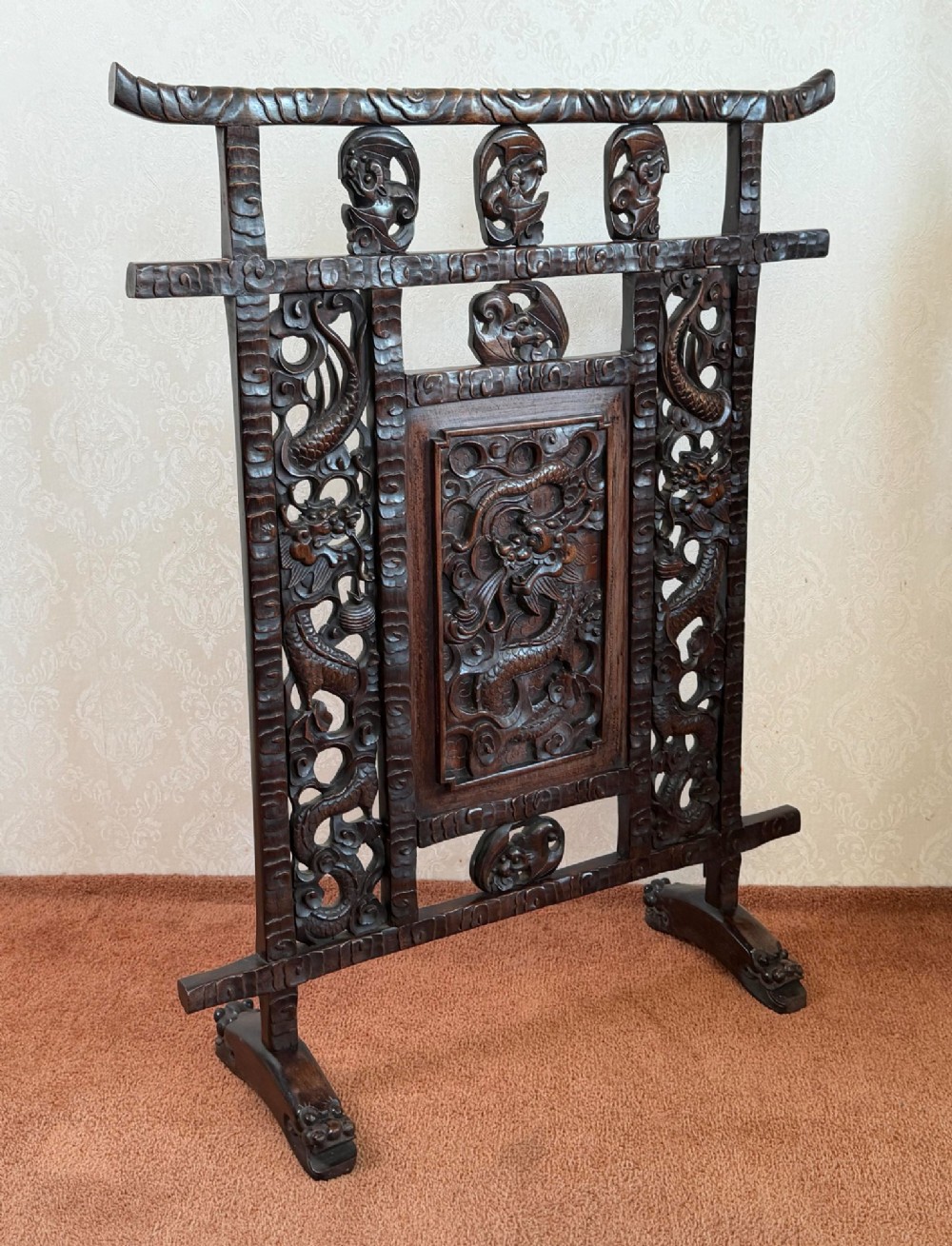 A dark carved hardwood freestanding screen featuring openwork dragon motifs and a central relief panel on carved feet. View III