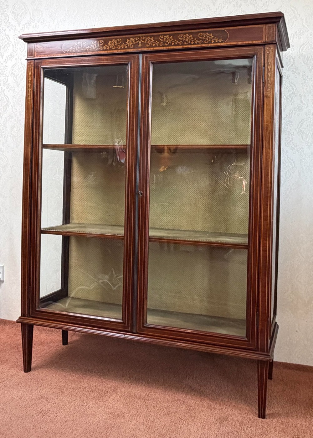 A late nineteenth-century mahogany display cabinet featuring twin glazed doors, floral marquetry frieze inlay, glass side panels, and square tapered legs.
