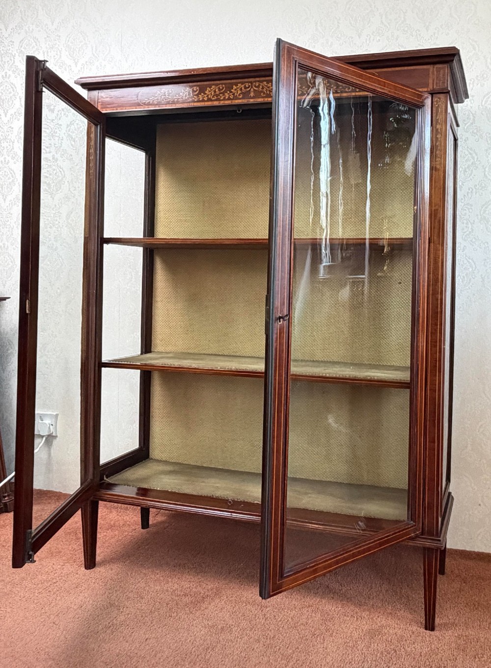 A late nineteenth-century mahogany display cabinet featuring twin glazed doors, floral marquetry frieze inlay, glass side panels, and square tapered legs. View II