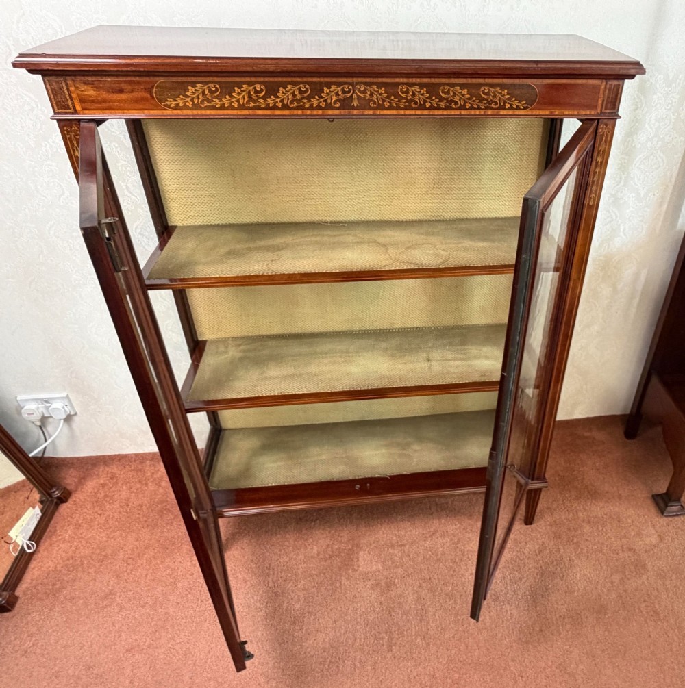 A late nineteenth-century mahogany display cabinet featuring twin glazed doors, floral marquetry frieze inlay, glass side panels, and square tapered legs. View IV