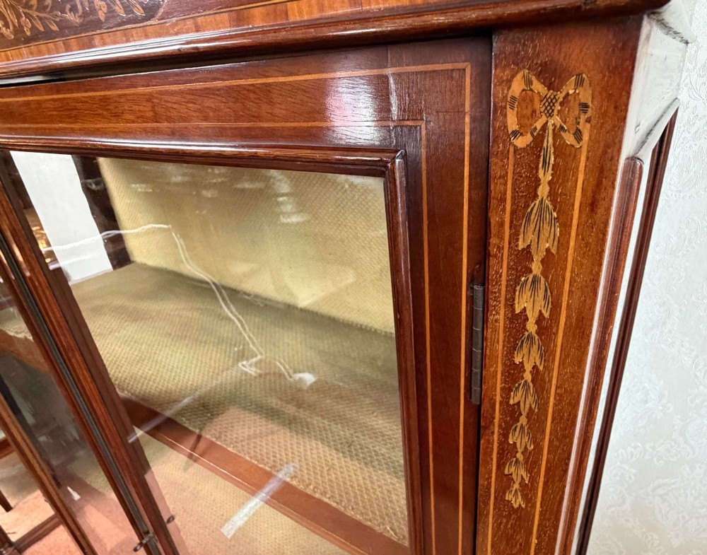 A late nineteenth-century mahogany display cabinet featuring twin glazed doors, floral marquetry frieze inlay, glass side panels, and square tapered legs. View VI