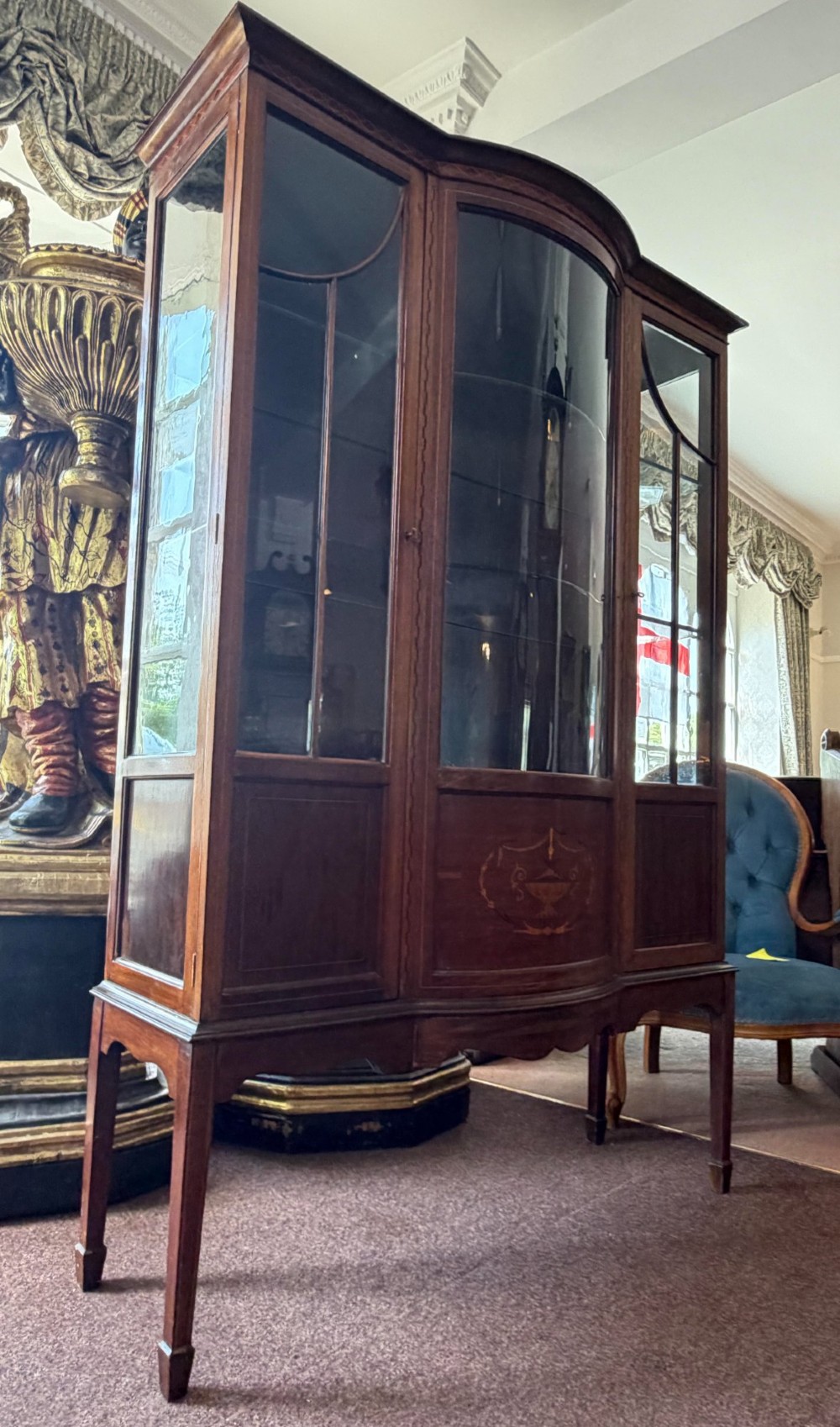 A late Victorian mahogany bow-front display cabinet featuring glazed doors, detailed marquetry inlay, and raised square tapered legs.