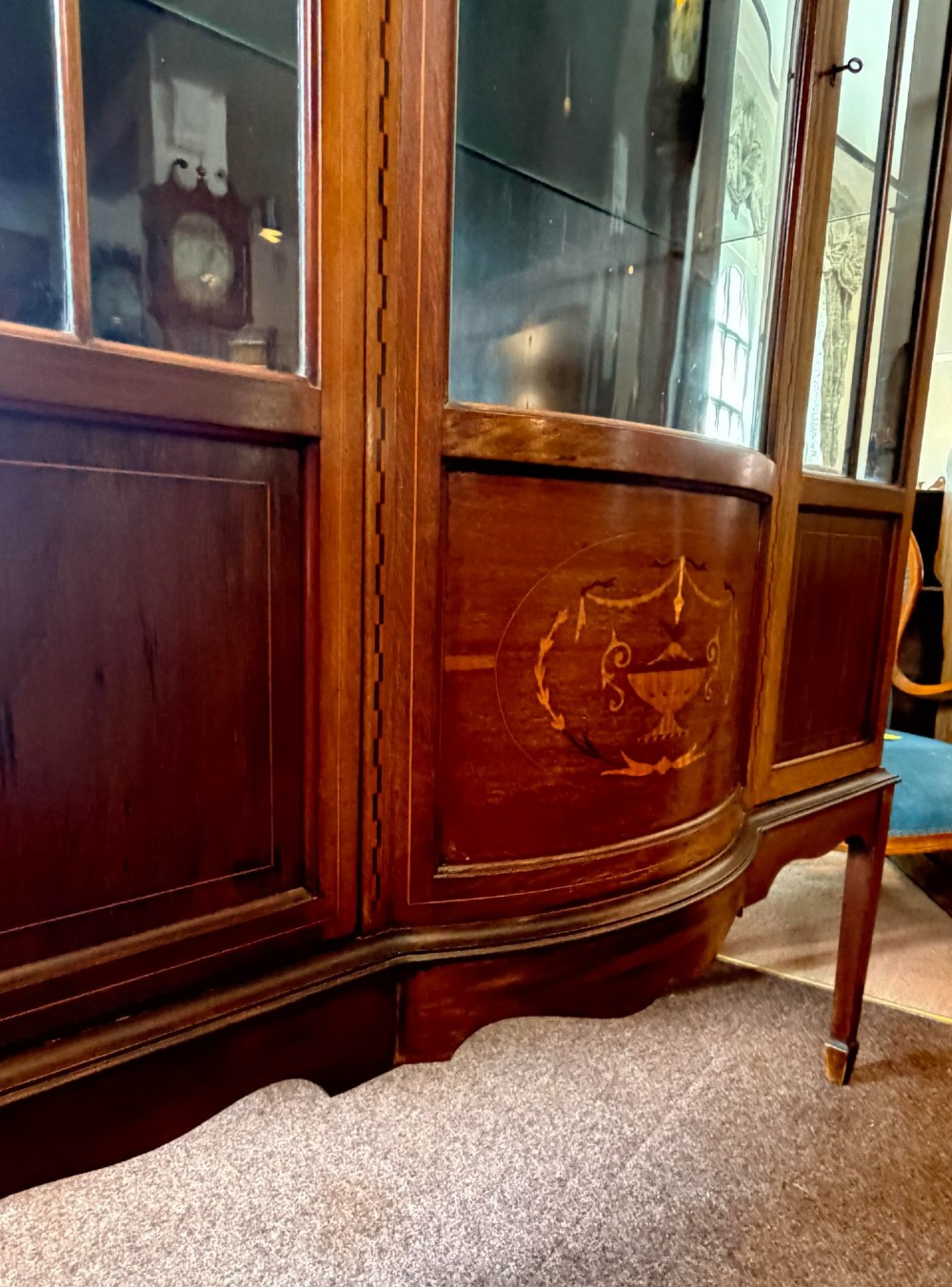 A late Victorian mahogany bow-front display cabinet featuring glazed doors, detailed marquetry inlay, and raised square tapered legs. View II