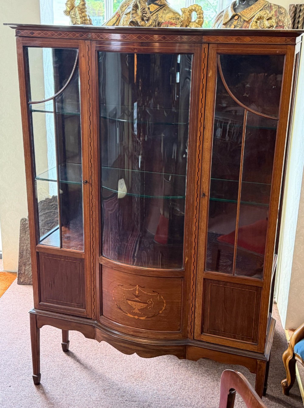 A late Victorian mahogany bow-front display cabinet featuring glazed doors, detailed marquetry inlay, and raised square tapered legs. View V