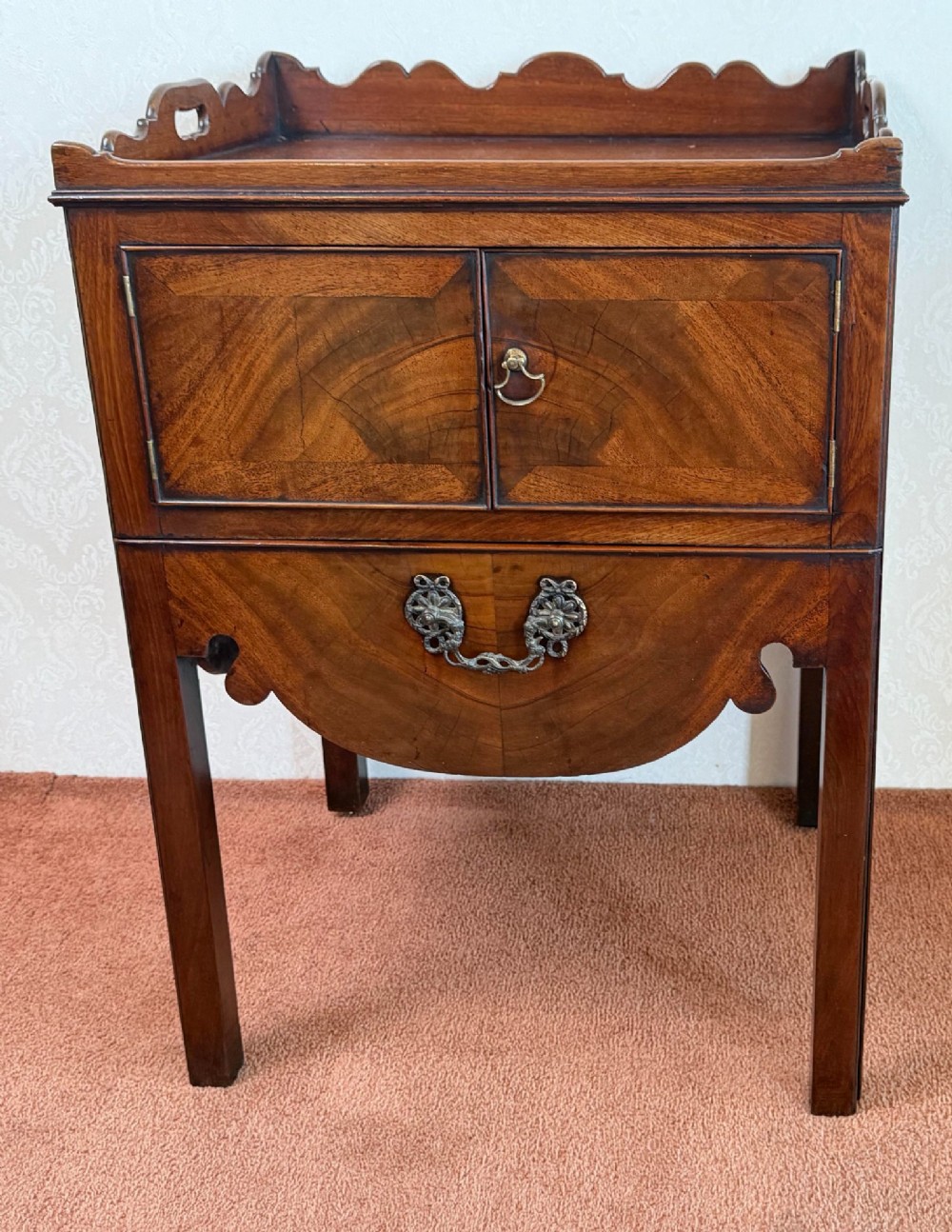 Mid-18th century Georgian mahogany bedside cabinet featuring a tray top gallery with cut-out handholds, double cupboard doors, lower drawer, and square legs.