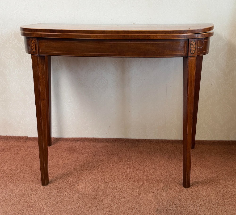 A Sheraton period mahogany tea table with a semi-circular folding top, string inlay along the apron, and slender square tapered legs.