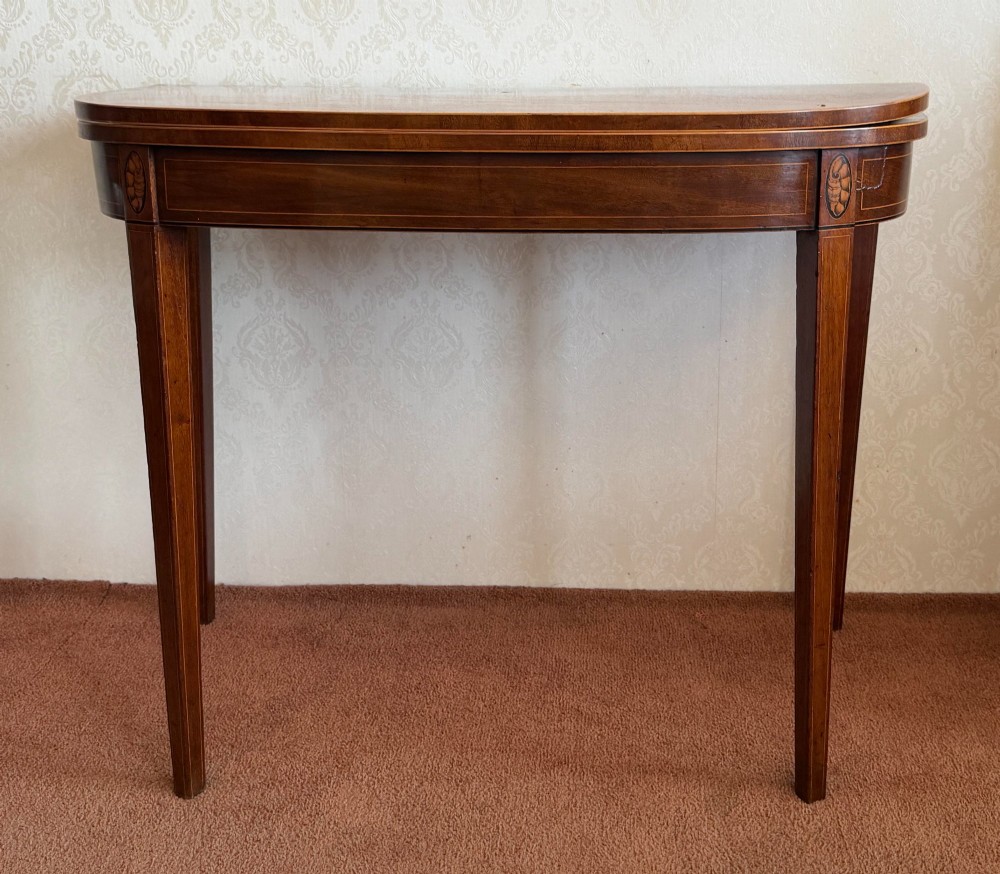 A Sheraton period mahogany tea table with a semi-circular folding top, string inlay along the apron, and slender square tapered legs. View II