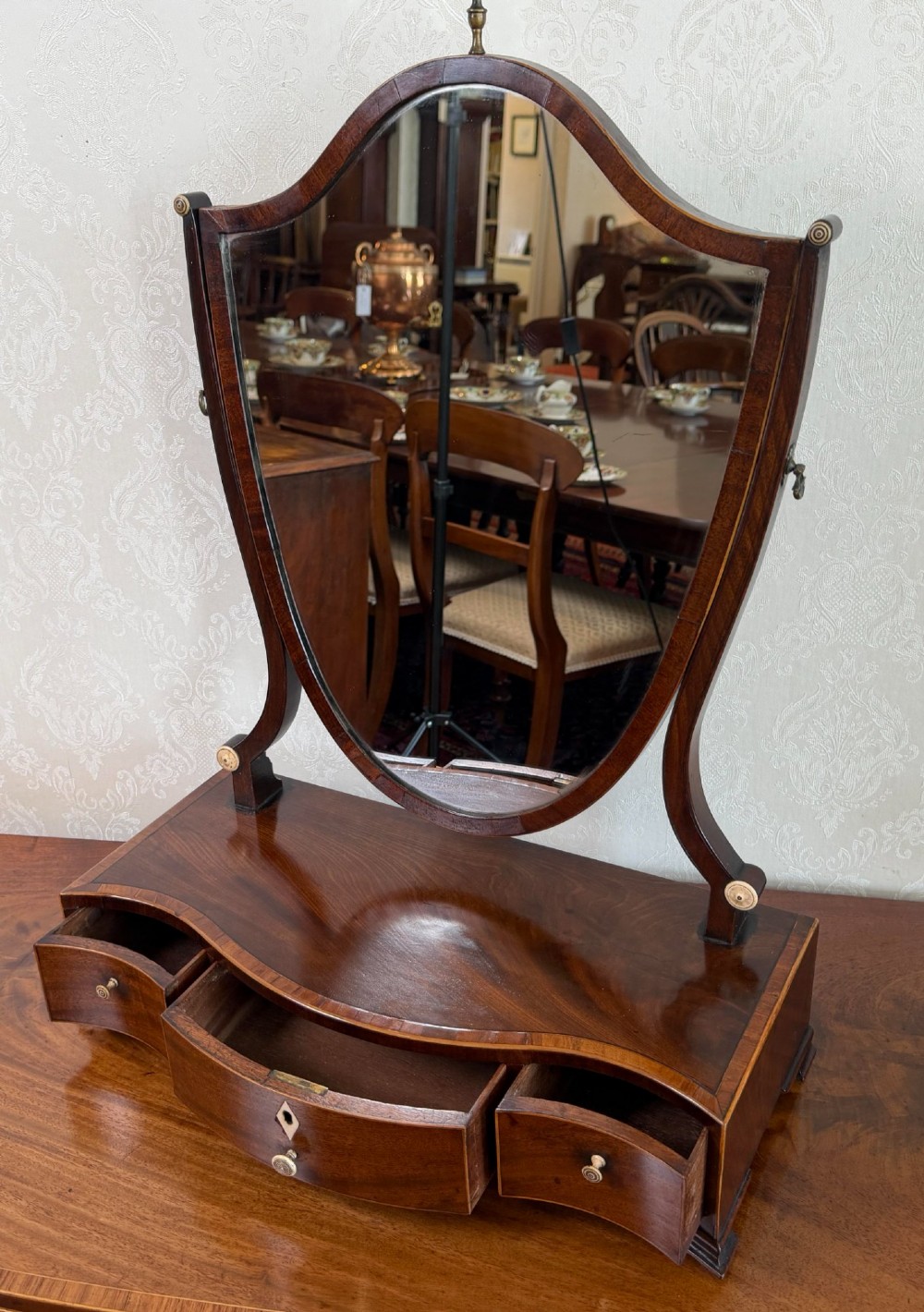 A Regency mahogany box dressing mirror with an oval swing frame supported above a serpentine base with three drawers. View II
