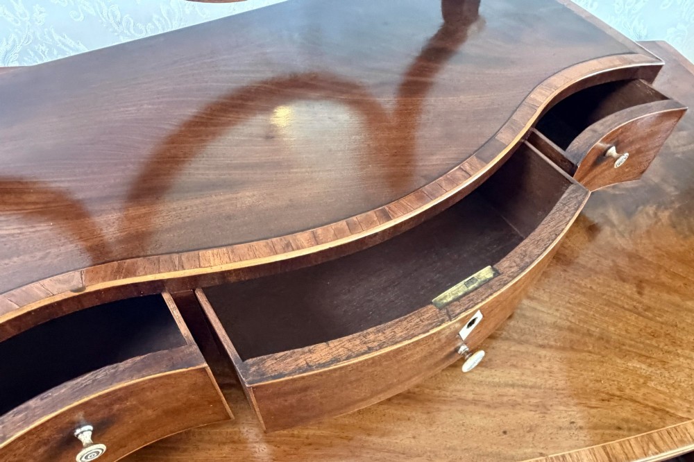 A Regency mahogany box dressing mirror with an oval swing frame supported above a serpentine base with three drawers. View IV
