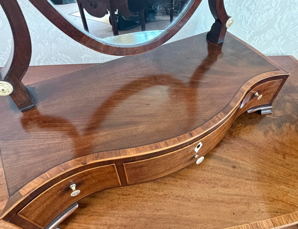 A Regency mahogany box dressing mirror with an oval swing frame supported above a serpentine base with three drawers. View V