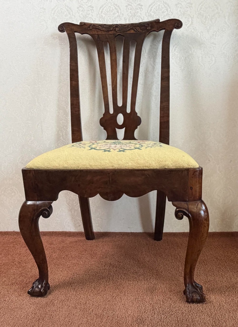An early 18th-century walnut side chair featuring a carved pierced splat back, shaped apron, cabriole front legs, and an embroidered drop-in seat pad.
