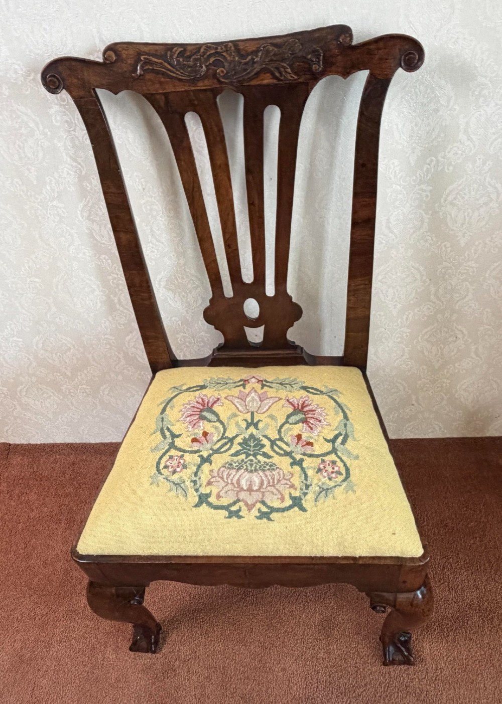 An early 18th-century walnut side chair featuring a carved pierced splat back, shaped apron, cabriole front legs, and an embroidered drop-in seat pad. View VI