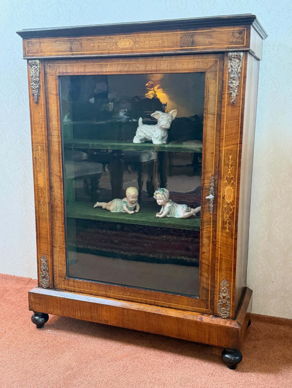 A Victorian burr walnut pier cabinet with floral marquetry inlay, ornate gilt brass mounts, and a single glazed door disclosing velvet-lined shelving.