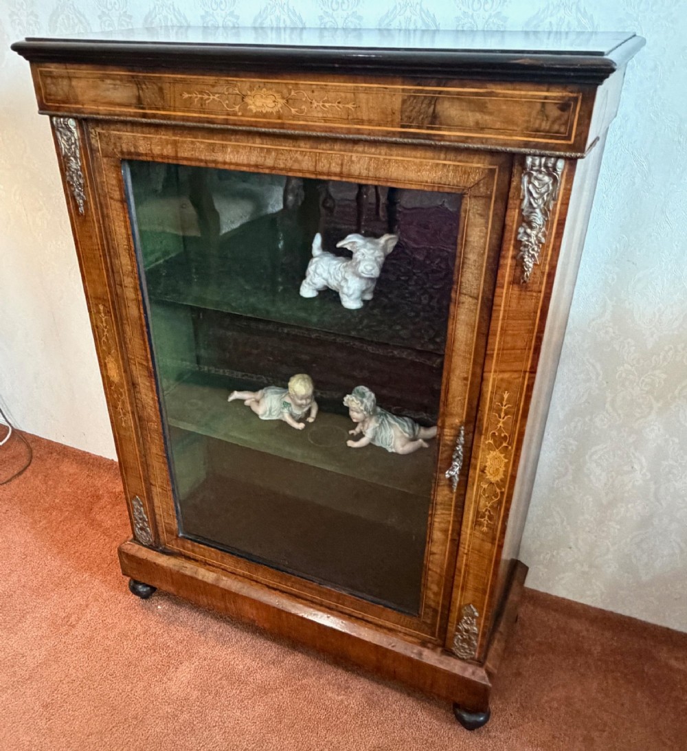 A Victorian burr walnut pier cabinet with floral marquetry inlay, ornate gilt brass mounts, and a single glazed door disclosing velvet-lined shelving. View VIII