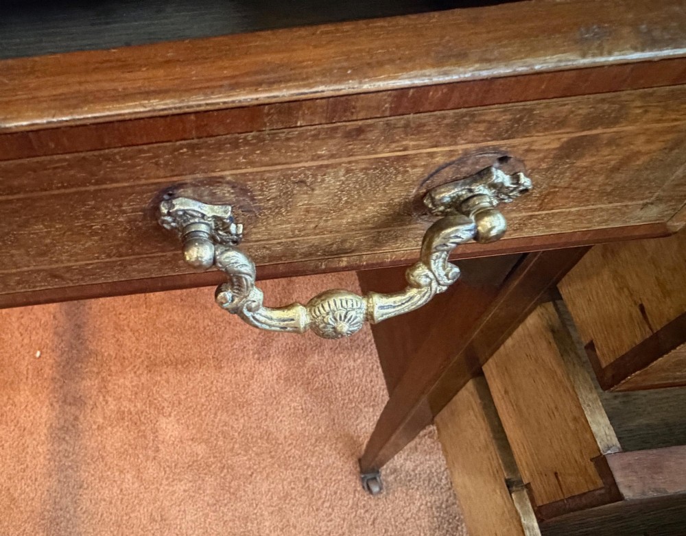 An antique mahogany kneehole writing desk featuring a green leather top surface, inlaid stringing, five drawers with brass handles, and square tapered legs on castors. View VII