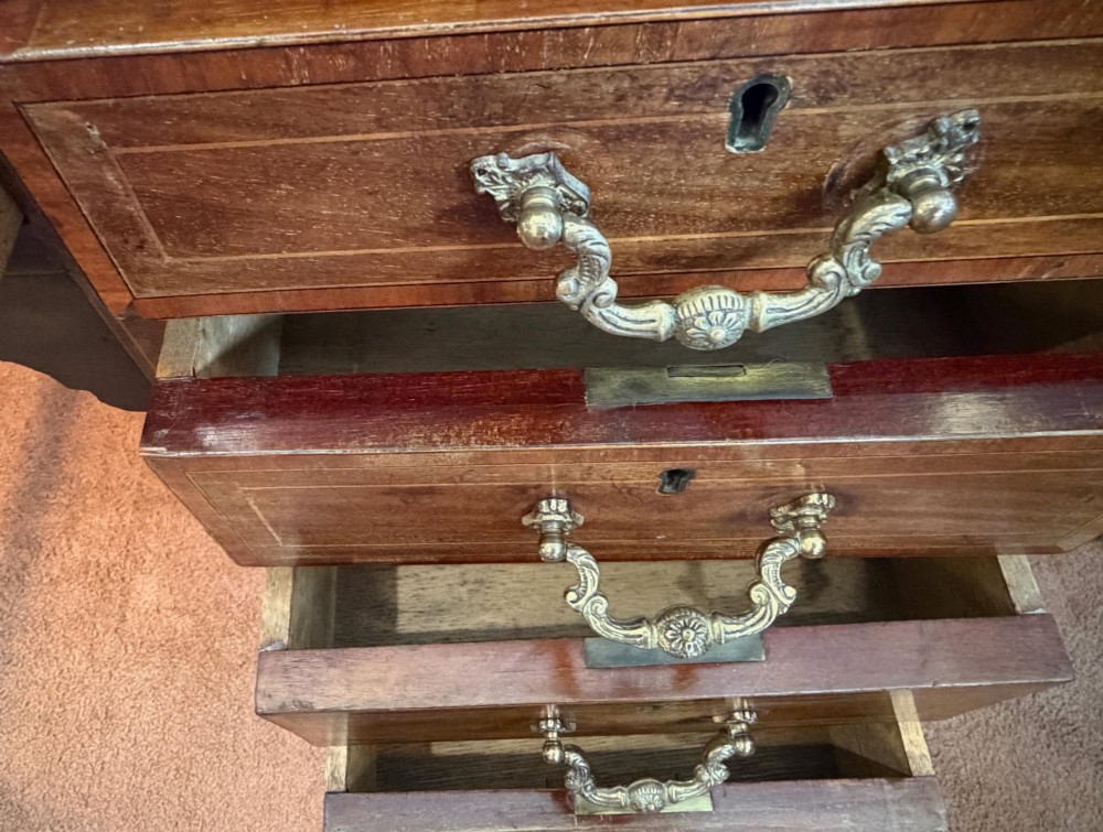 An antique mahogany kneehole writing desk featuring a green leather top surface, inlaid stringing, five drawers with brass handles, and square tapered legs on castors. View VIII