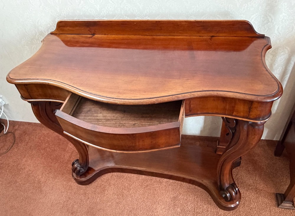 A Victorian mahogany serpentine console table featuring carved S-scroll legs, a low splashback upstand, and a shaped plinth base. View III