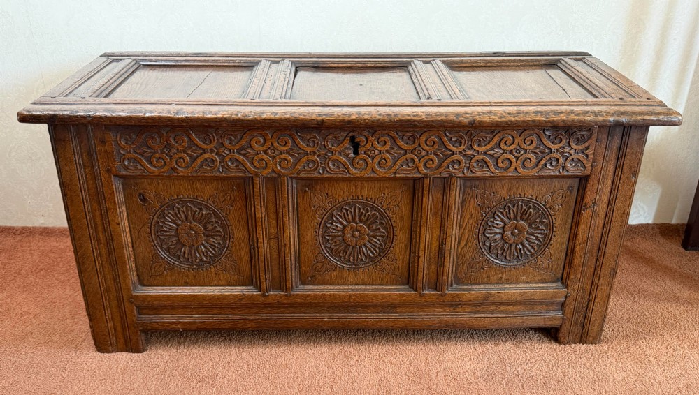 A 17th-century English oak coffer featuring a three-panel front carved with floral rosettes, an upper carved frieze, and a panelled lid.
