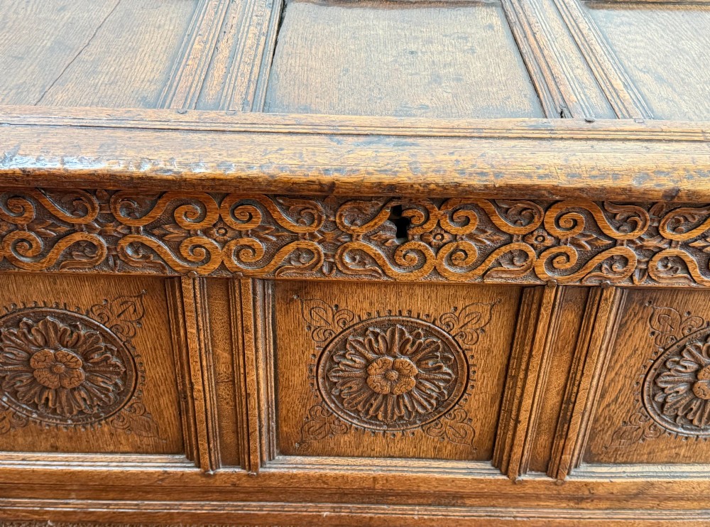 A 17th-century English oak coffer featuring a three-panel front carved with floral rosettes, an upper carved frieze, and a panelled lid. View II