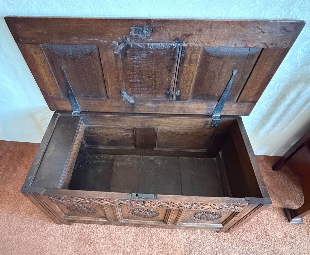 A 17th-century English oak coffer featuring a three-panel front carved with floral rosettes, an upper carved frieze, and a panelled lid. View IV