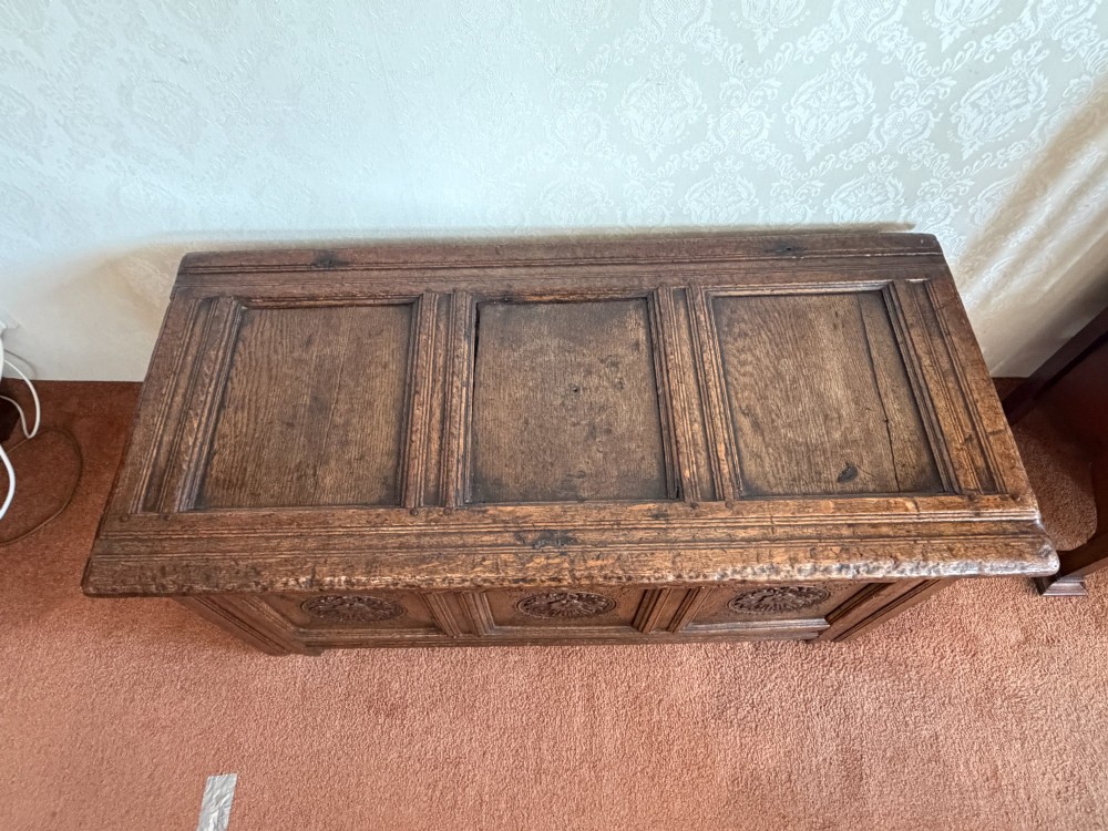 A 17th-century English oak coffer featuring a three-panel front carved with floral rosettes, an upper carved frieze, and a panelled lid. View V