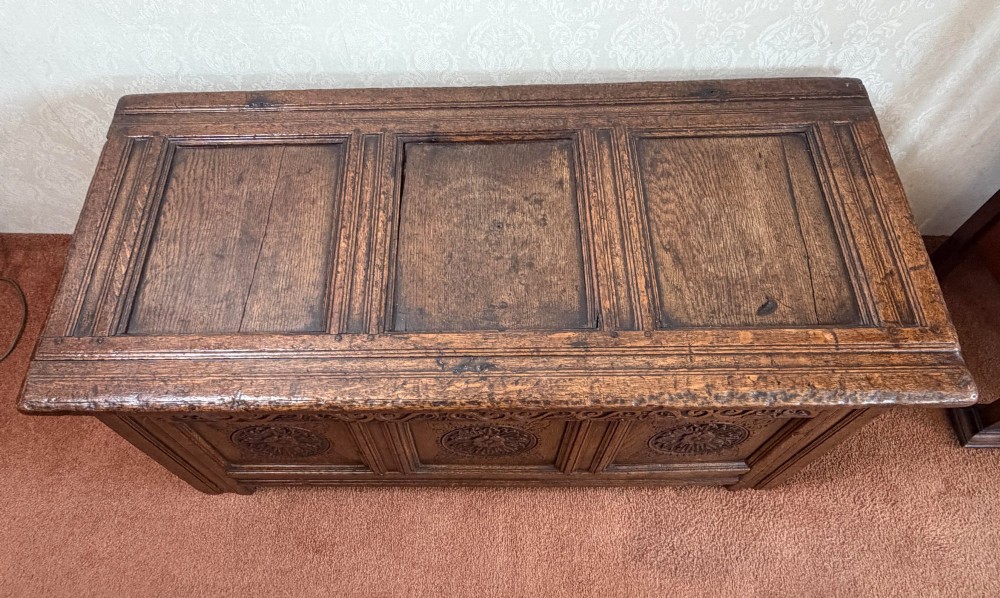 A 17th-century English oak coffer featuring a three-panel front carved with floral rosettes, an upper carved frieze, and a panelled lid. View VI