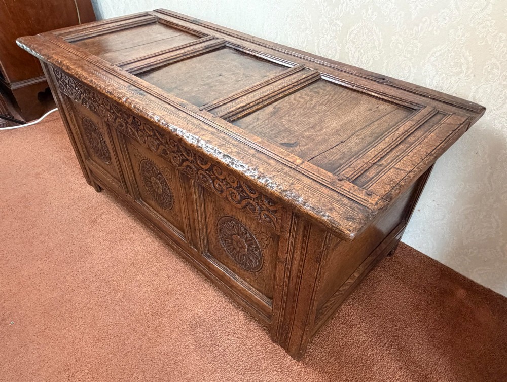 A 17th-century English oak coffer featuring a three-panel front carved with floral rosettes, an upper carved frieze, and a panelled lid. View VII