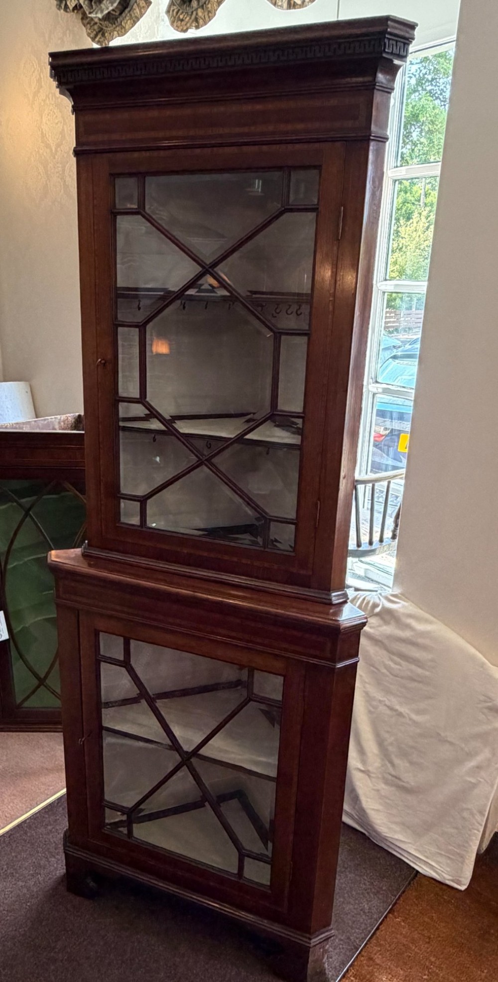 A tall two-tier mahogany corner cabinet featuring geometric glass door panes, satinwood inlay details, and bracket feet. View III