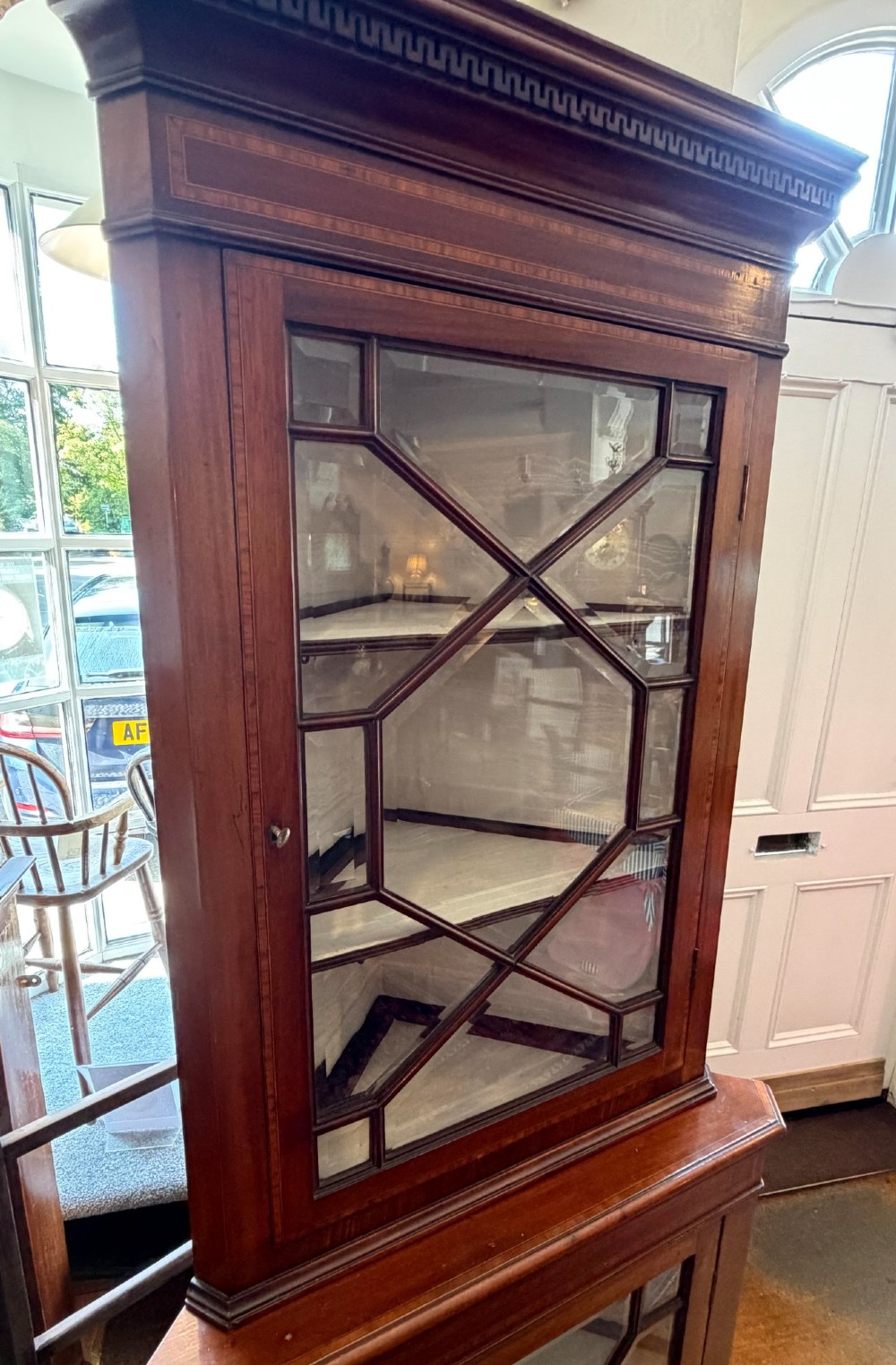 A tall two-tier mahogany corner cabinet featuring geometric glass door panes, satinwood inlay details, and bracket feet. View IV