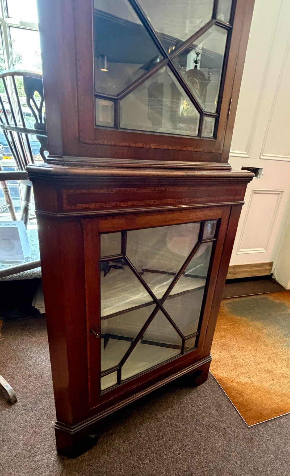 A tall two-tier mahogany corner cabinet featuring geometric glass door panes, satinwood inlay details, and bracket feet. View V