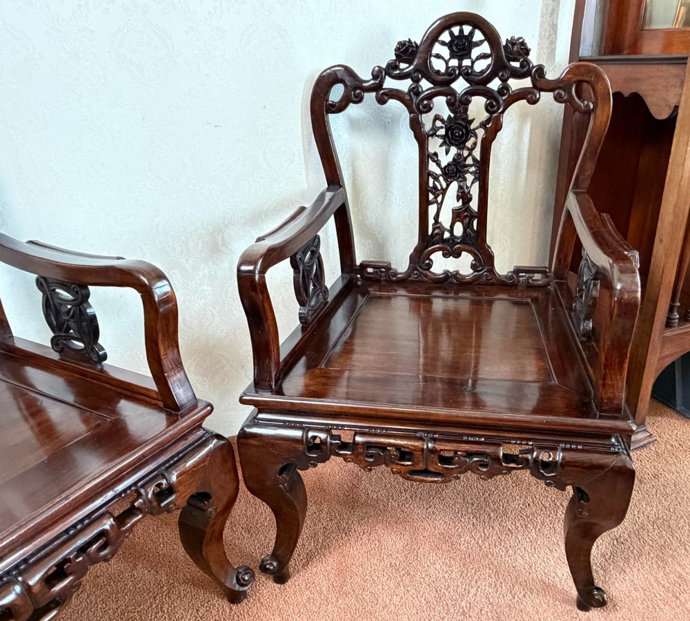 A pair of dark polished hardwood armchairs featuring intricate openwork floral carvings on the splat and decorative carved aprons. View II