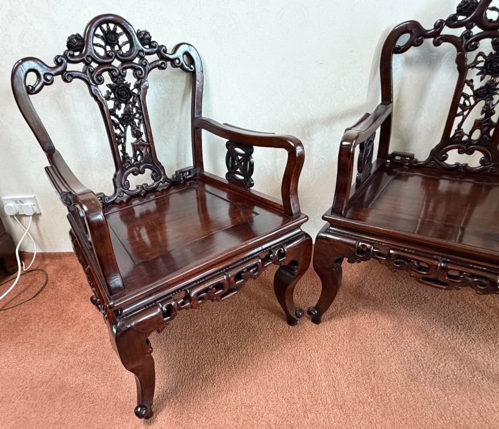 A pair of dark polished hardwood armchairs featuring intricate openwork floral carvings on the splat and decorative carved aprons. View III