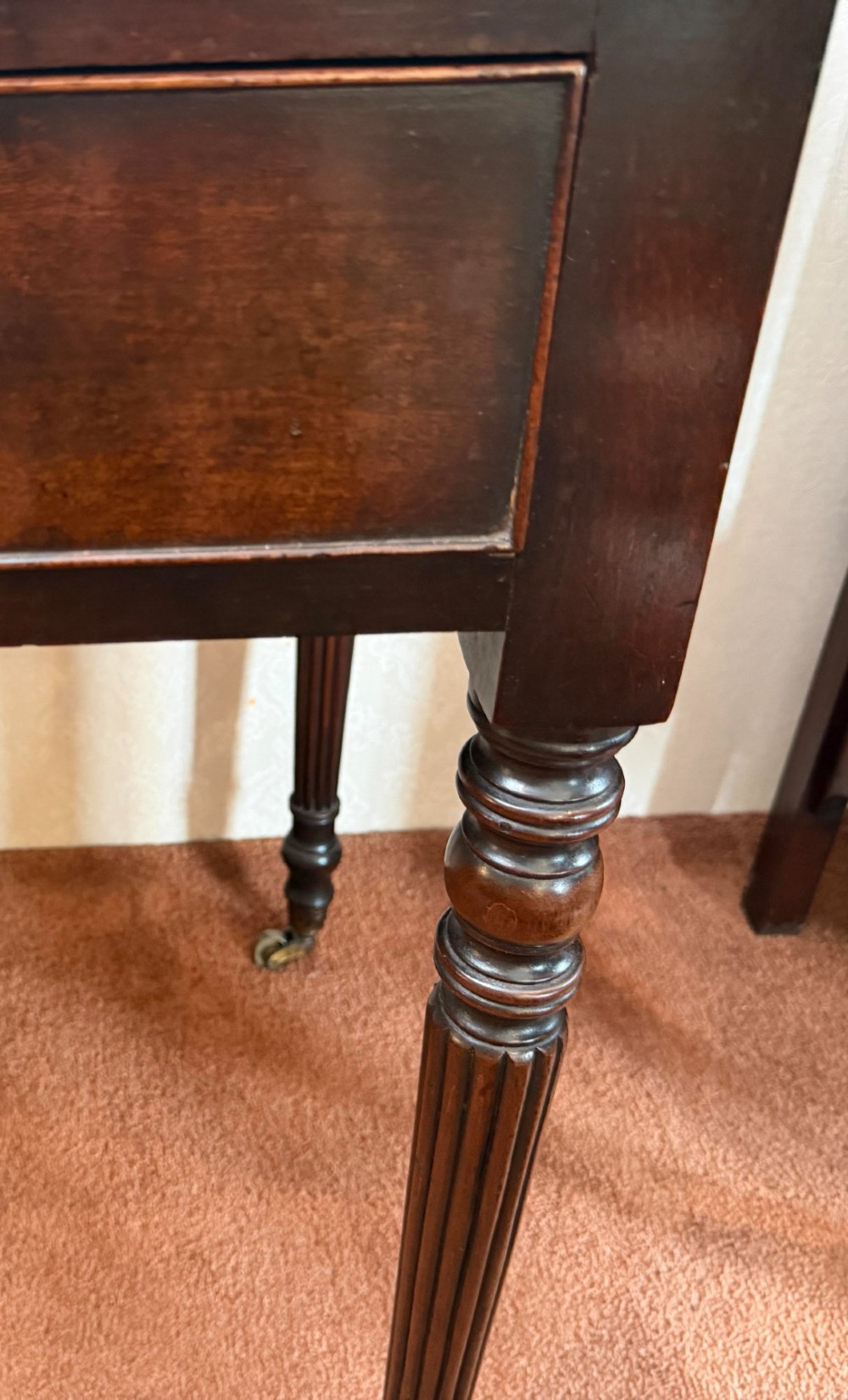 A dark mahogany writing table featuring a raised gallery back, three frieze drawers with turned wooden knobs, turned reeded legs, and brass castors. View V