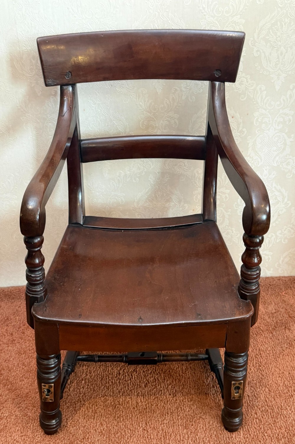 An antique dark mahogany childs armchair with turned support posts, scrolled armrests, a curved top rail, and a solid wooden seat. View II
