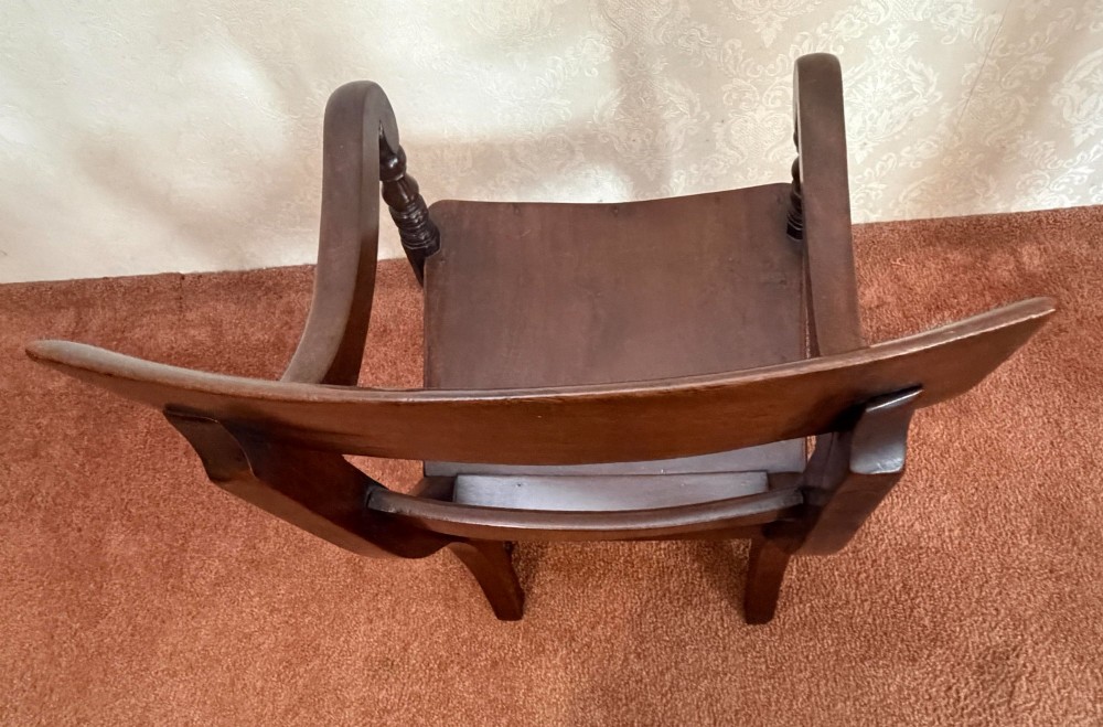 An antique dark mahogany childs armchair with turned support posts, scrolled armrests, a curved top rail, and a solid wooden seat. View V