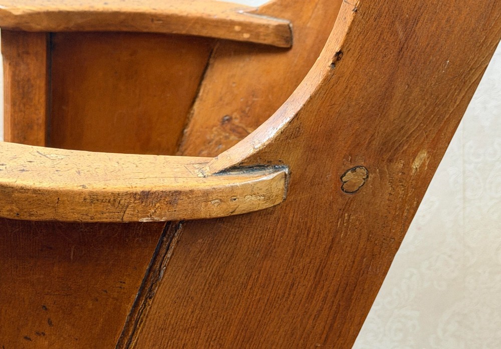 A small wooden antique childs rocking chair featuring solid enclosed panel sides, integrated armrests, and curved wooden rockers. View II