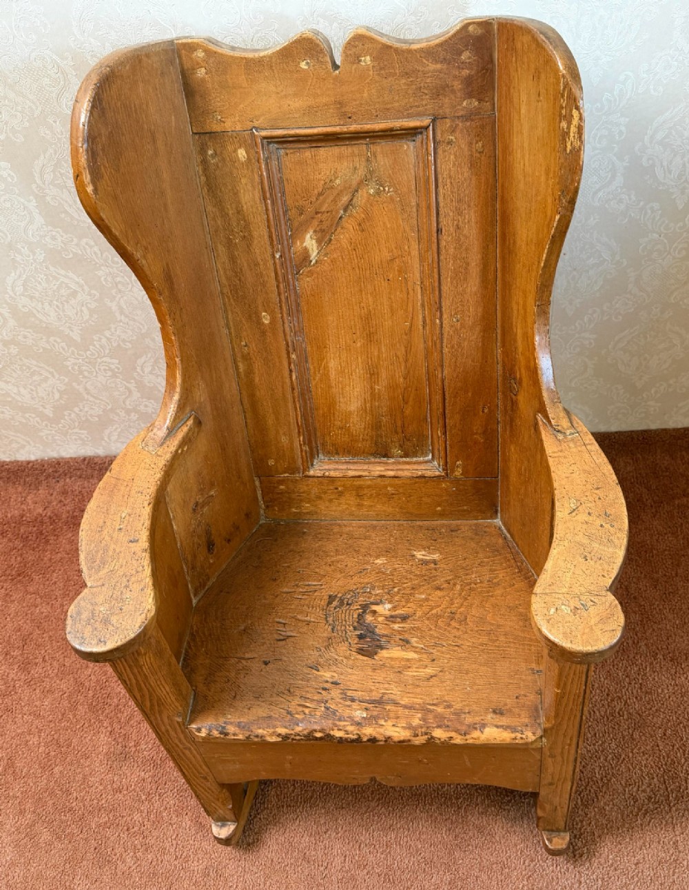 A small wooden antique childs rocking chair featuring solid enclosed panel sides, integrated armrests, and curved wooden rockers. View IV