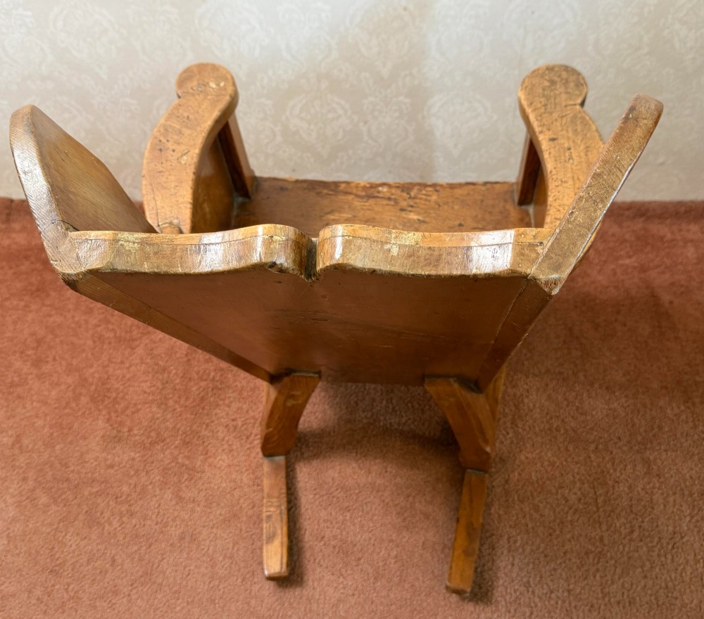 A small wooden antique childs rocking chair featuring solid enclosed panel sides, integrated armrests, and curved wooden rockers. View V