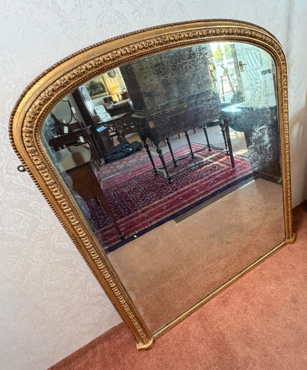 A Victorian arched overmantel mirror featuring a gilded wood frame with beaded moulding and foxed glass plate. View II