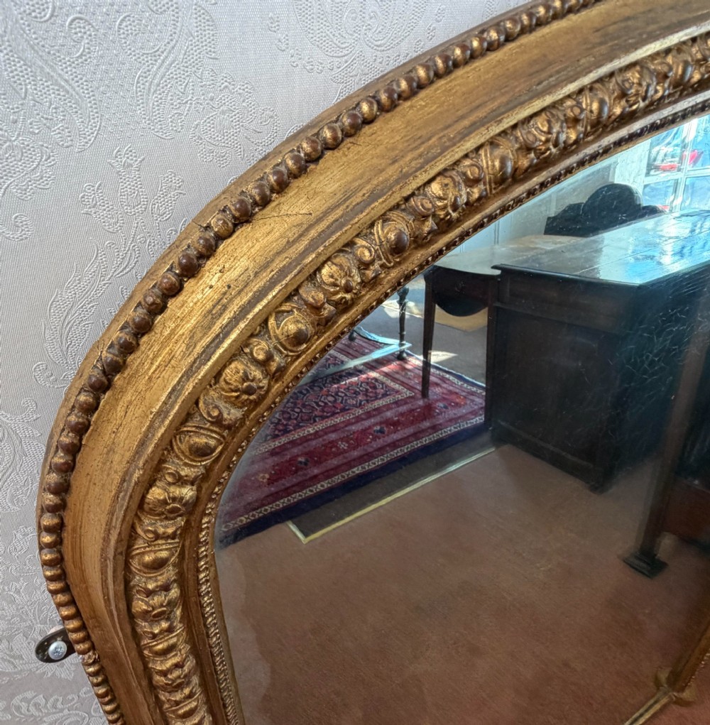 A Victorian arched overmantel mirror featuring a gilded wood frame with beaded moulding and foxed glass plate. View III
