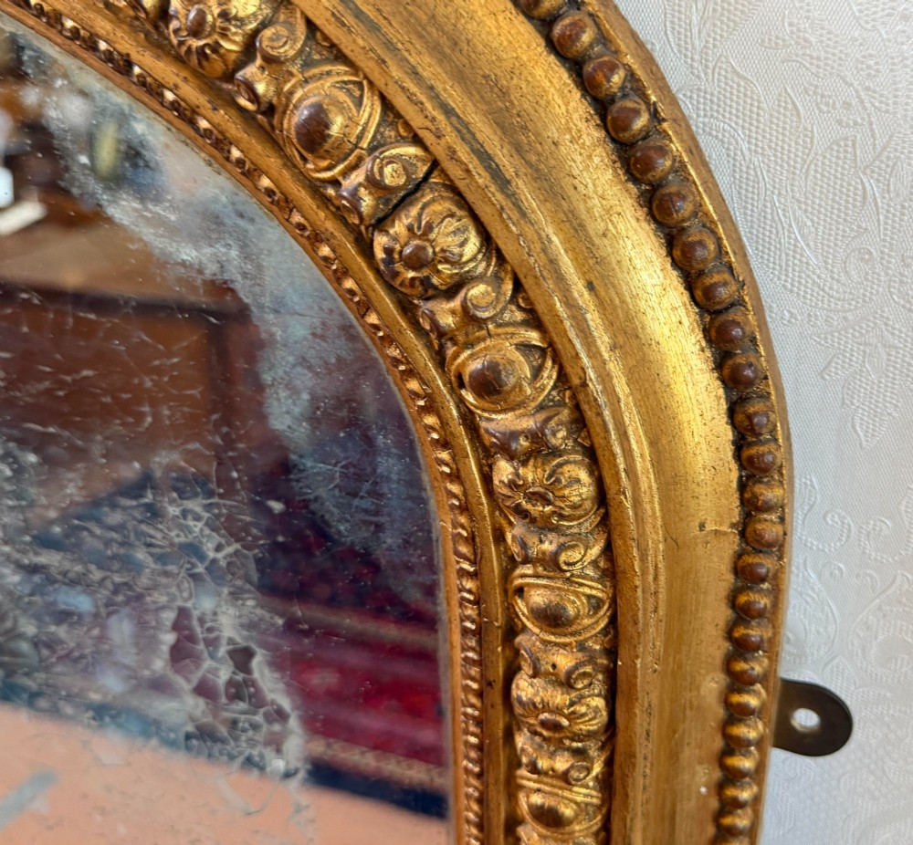 A Victorian arched overmantel mirror featuring a gilded wood frame with beaded moulding and foxed glass plate. View V