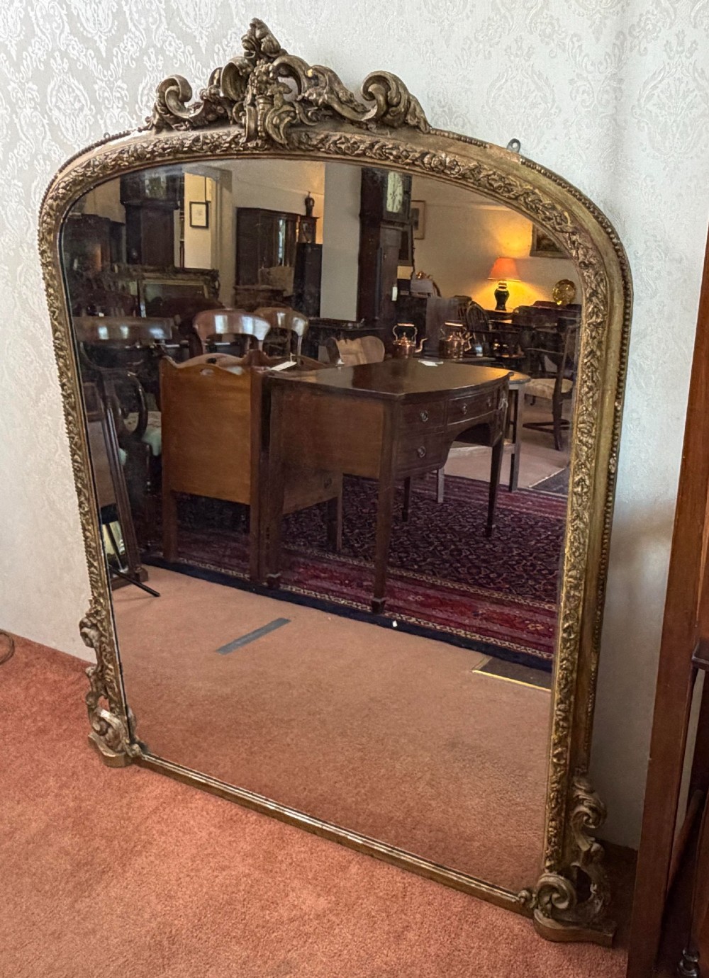 A large Victorian giltwood overmantel mirror featuring an arched top with detailed cresting, ornate scroll base spurs, and an embellished gilded frame. View II