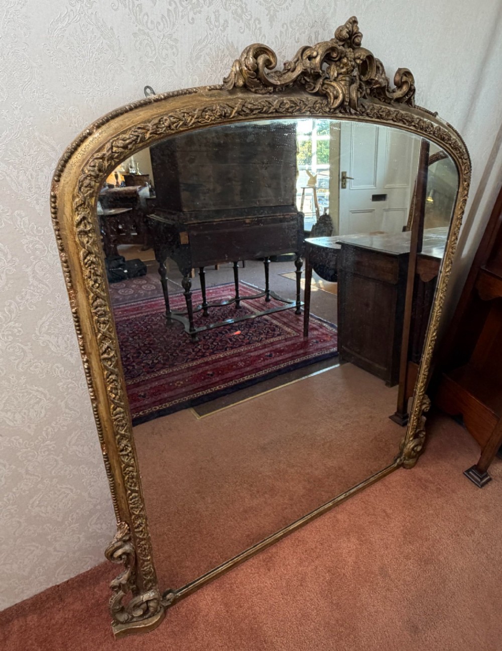 A large Victorian giltwood overmantel mirror featuring an arched top with detailed cresting, ornate scroll base spurs, and an embellished gilded frame. View V
