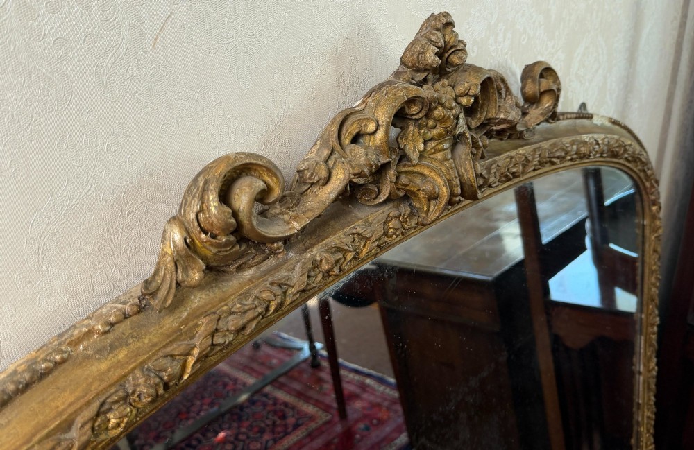 A large Victorian giltwood overmantel mirror featuring an arched top with detailed cresting, ornate scroll base spurs, and an embellished gilded frame. View VII