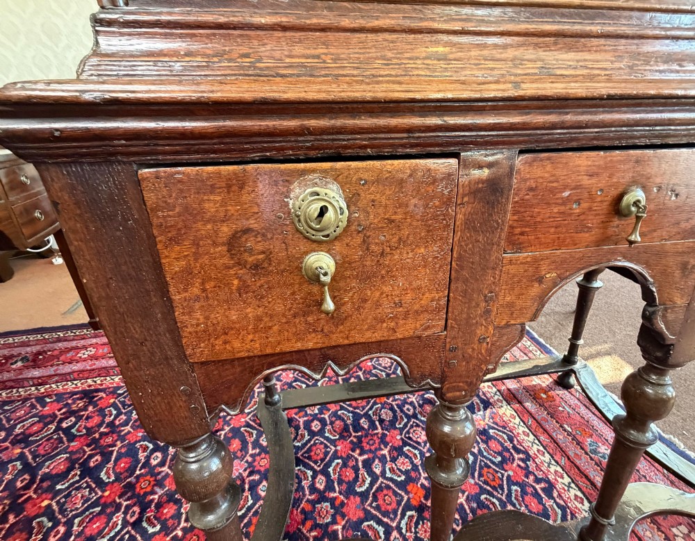 A mid 18th century dark oak chest on stand featuring multiple drawers, brass drop handles, a shaped lower apron, and turned legs with stretchers. View V