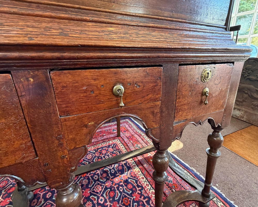 A mid 18th century dark oak chest on stand featuring multiple drawers, brass drop handles, a shaped lower apron, and turned legs with stretchers. View VI