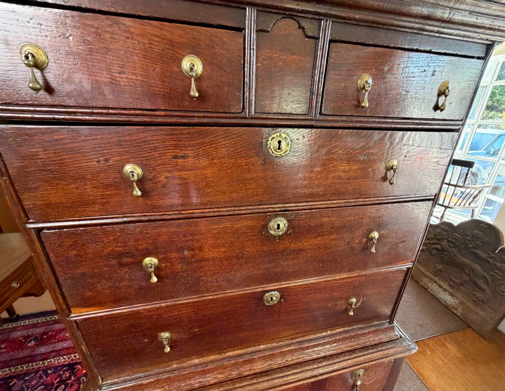 A mid 18th century dark oak chest on stand featuring multiple drawers, brass drop handles, a shaped lower apron, and turned legs with stretchers. View VII