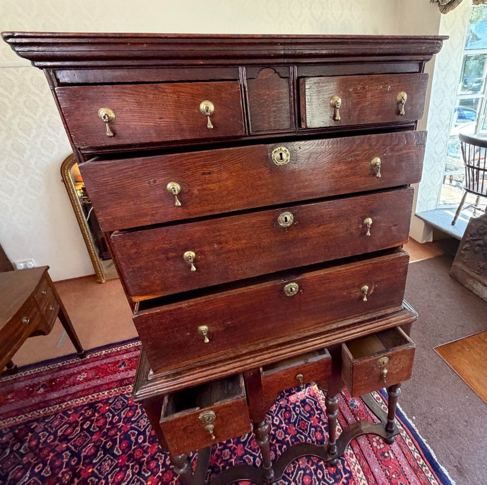 A mid 18th century dark oak chest on stand featuring multiple drawers, brass drop handles, a shaped lower apron, and turned legs with stretchers. View VIII